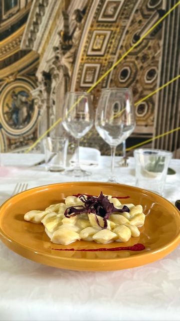 Un piatto di pasta arancione con guarnizione viola su un tavolo bianco in un ristorante sfarzoso.