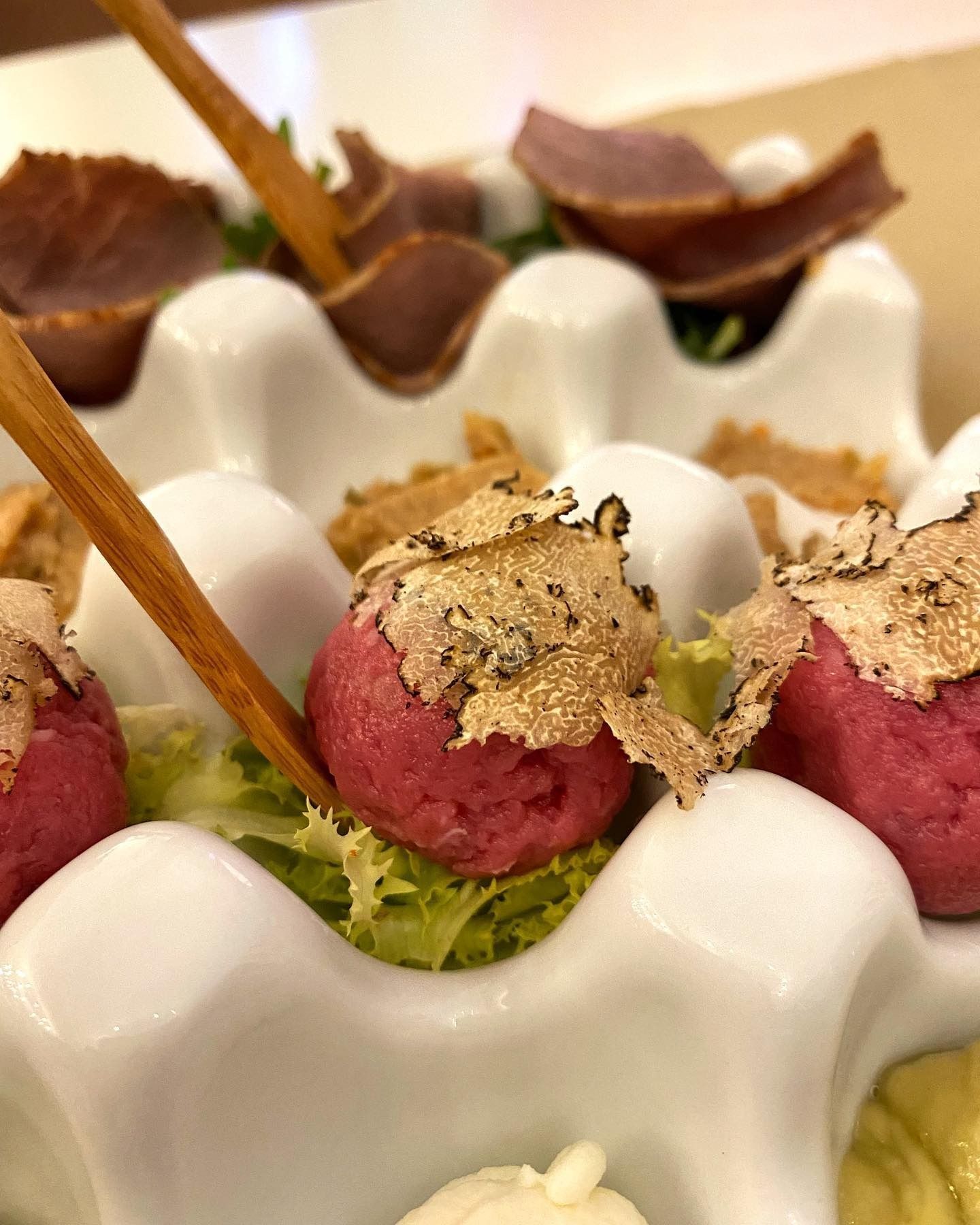 Antipasto di conchiglie di capesante bianche guarnite con palline di gelato rosa e verdi e decorazioni a scaglie, infilzate su spiedini di legno.