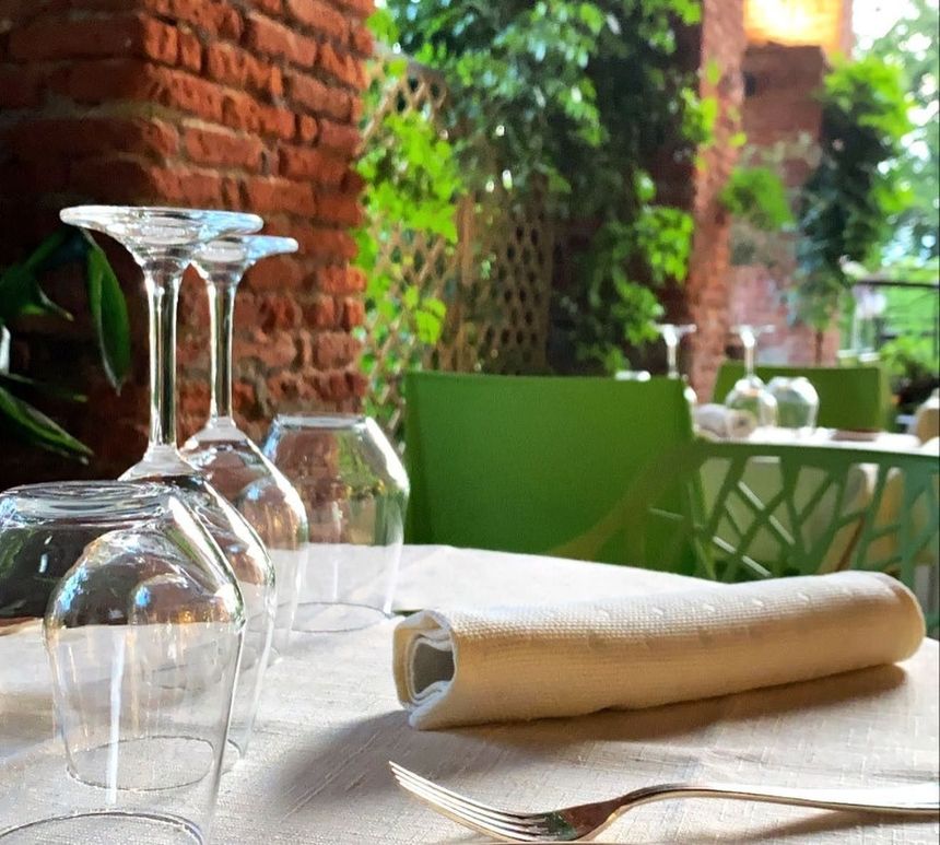 Apparecchiate la tavola con bicchieri da vino capovolti e tovaglioli arrotolati su un patio accanto a un muro di mattoni e al verde.