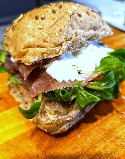 Primo piano di un panino al sesamo con verdure e carne a fette su un tagliere di legno.