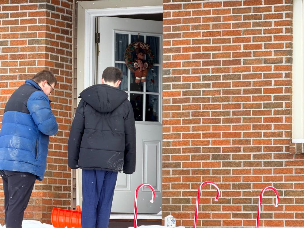Two people standing at a brick house doorway, looking at the door with red candy canes nearby.