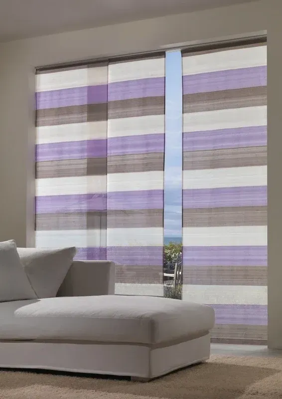 Soggiorno moderno con chaise longue grigia accanto a grandi tende trasparenti a righe viola.