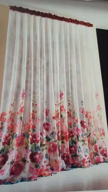 Tenda bianca trasparente con stampa floreale rosa lungo il bordo inferiore, appesa a una finestra.