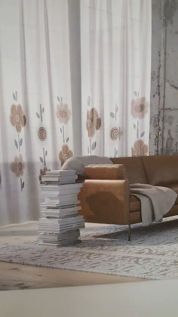 Accogliente soggiorno con divano beige, tappeto a motivi geometrici, tende che arrivano fino al pavimento e libri impilati accanto al divano.