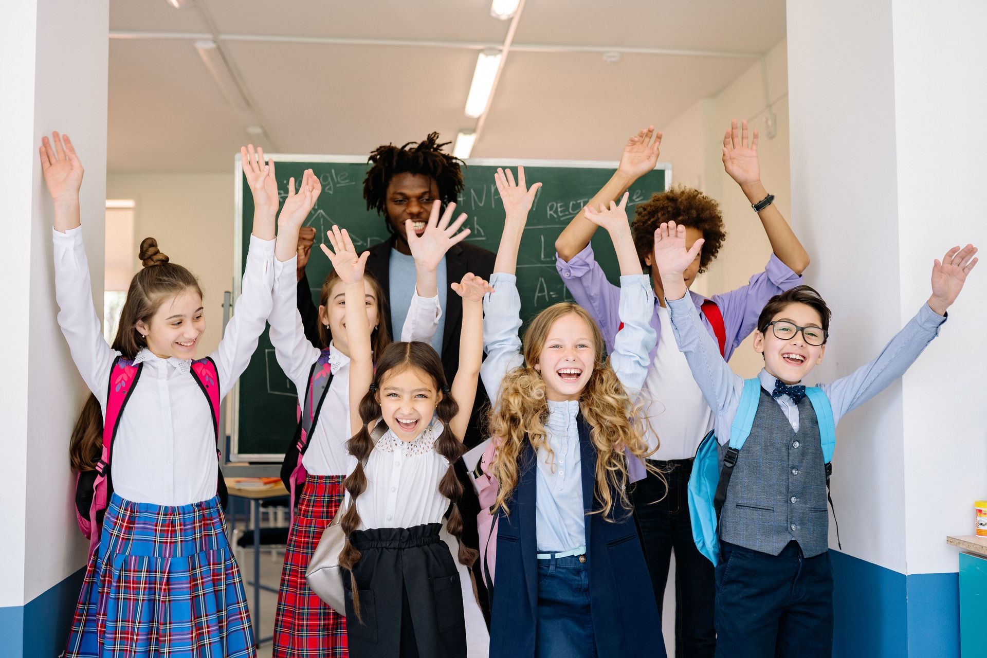 Children with raised arms in a classroom hallway, smiling and cheering