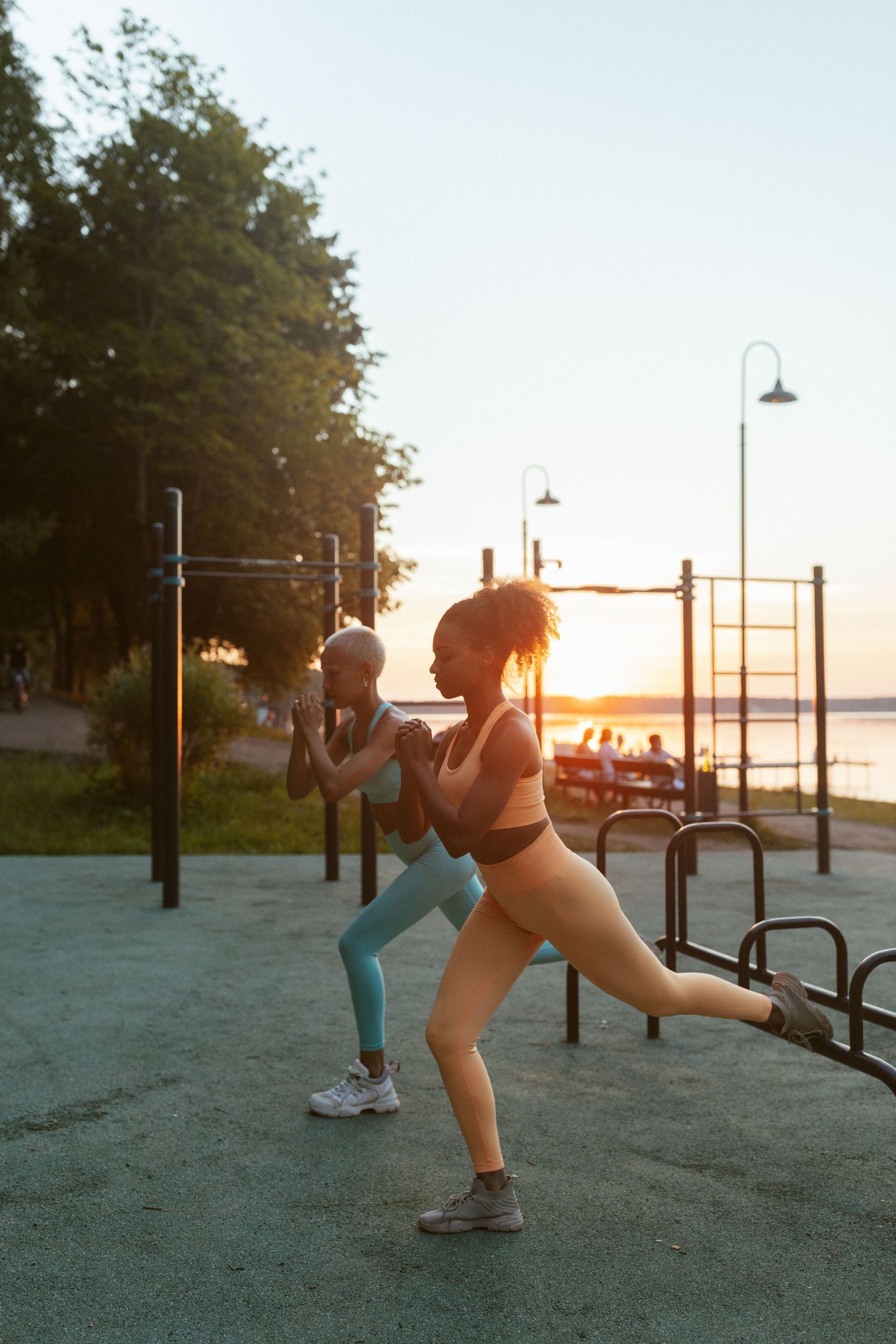 Two people exercising outdoors at sunset near a waterfront playground.