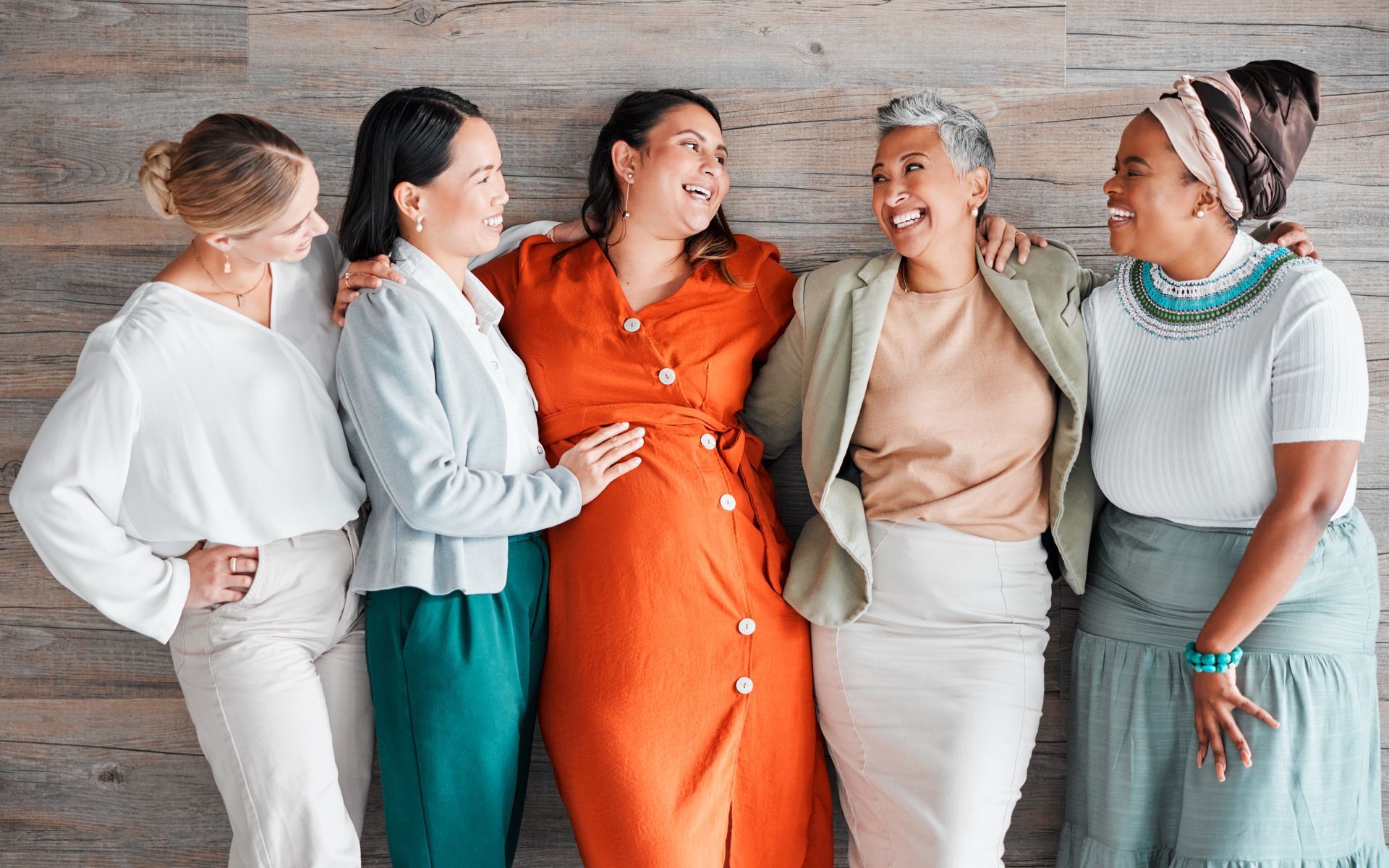 Five women together, dressed in coordinated colorful outfits against a light background