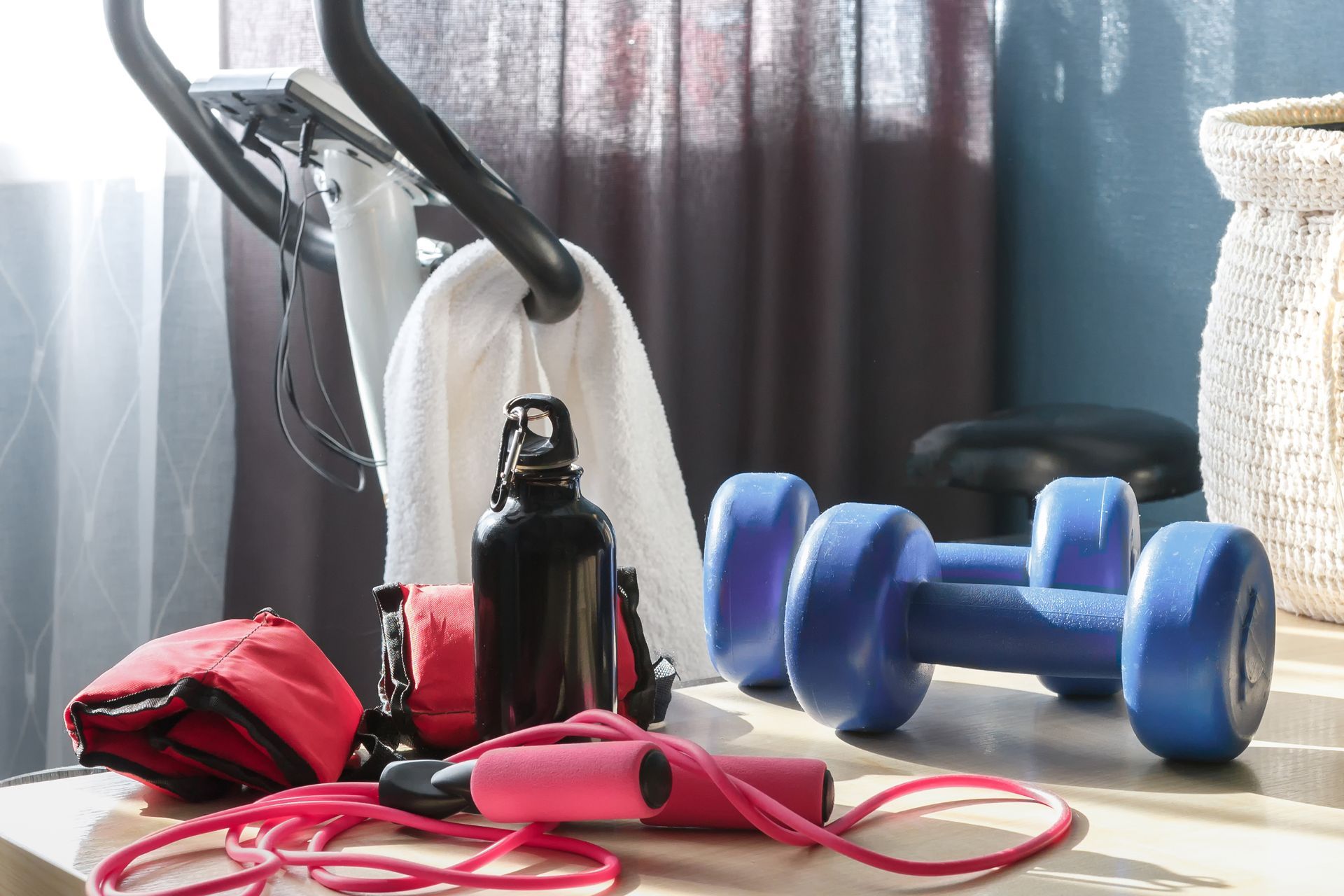 A table with dumbbells , a jump rope , a water bottle and a towel on it.