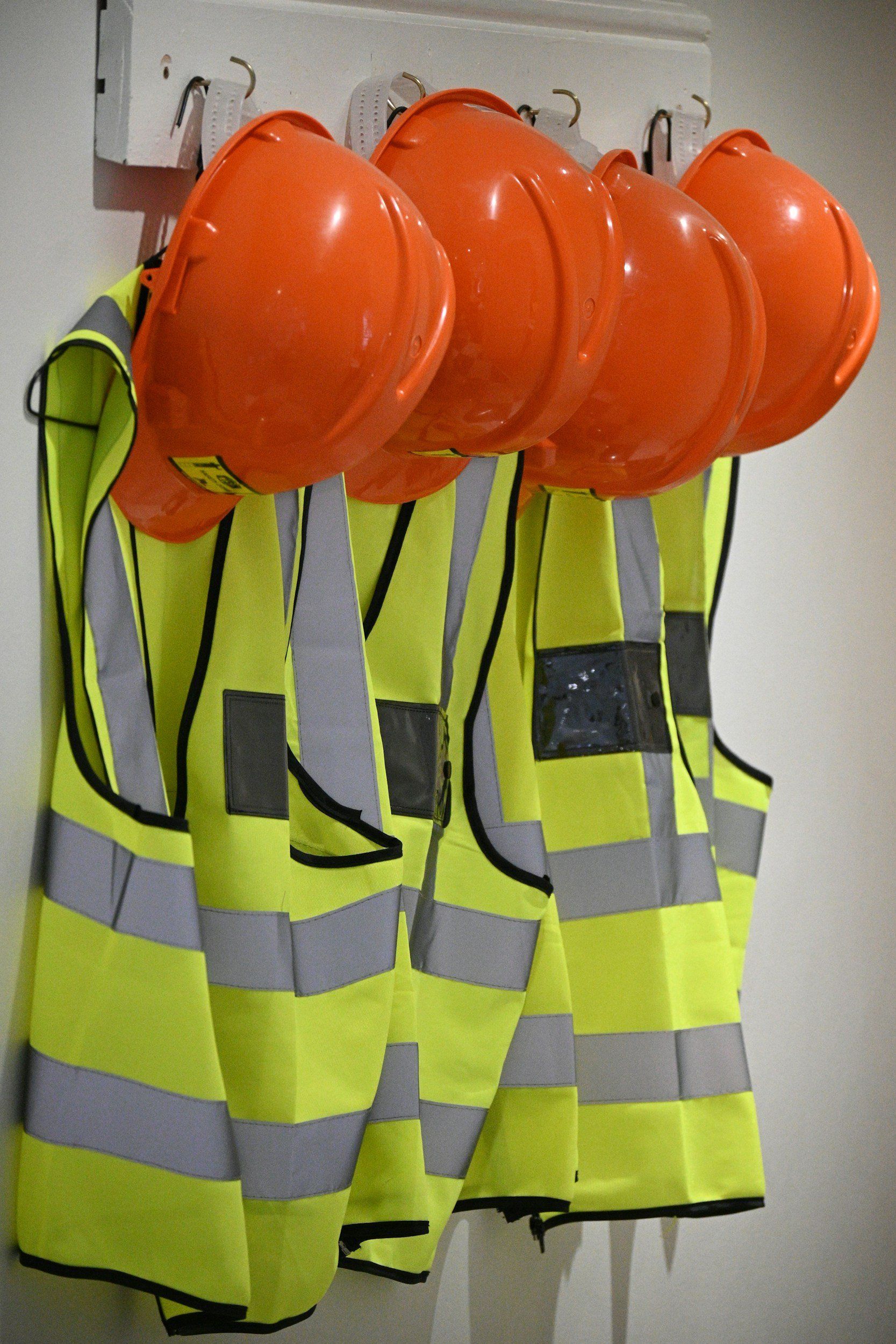 Orange hard hats and yellow safety vests hanging on hooks.