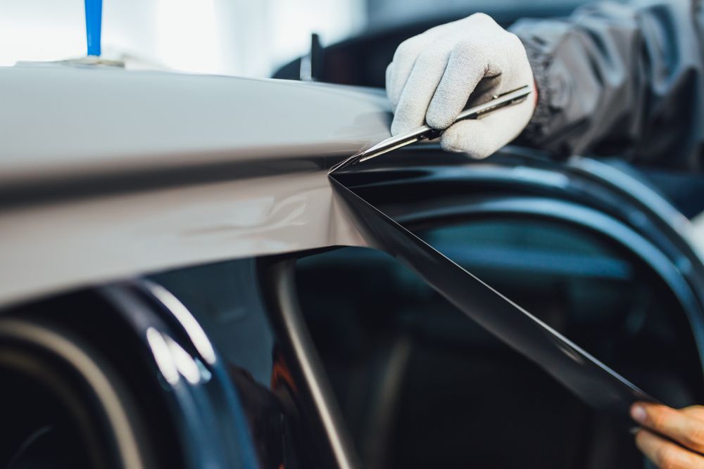 Person in gloves using a blade to trim window tint on a car.