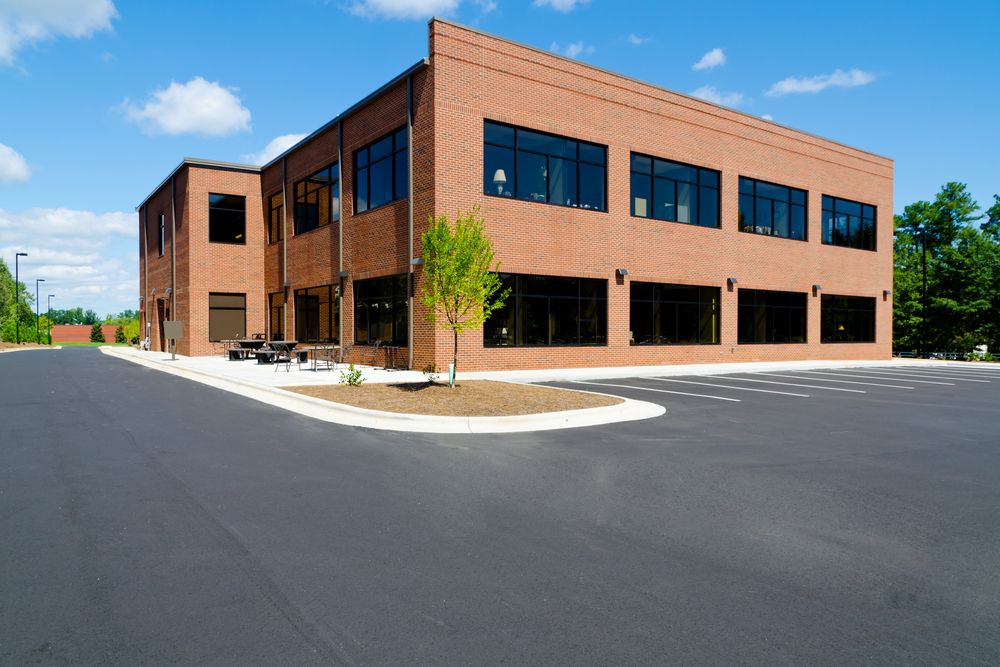 Brick office building with large windows, paved parking lot, and blue sky.