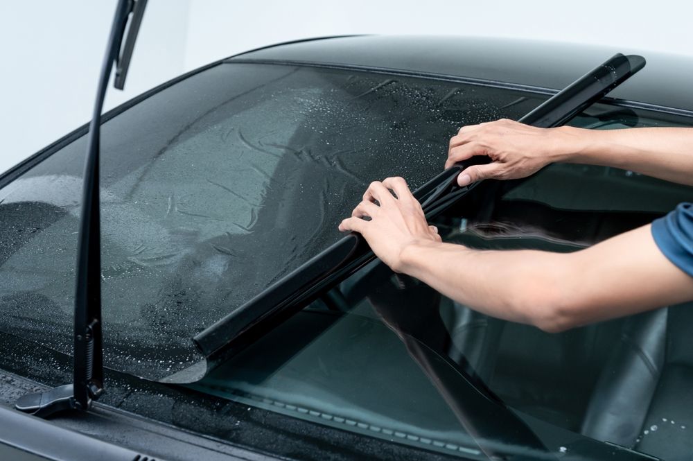 Hands replacing a windshield wiper blade on a car's wet windshield.