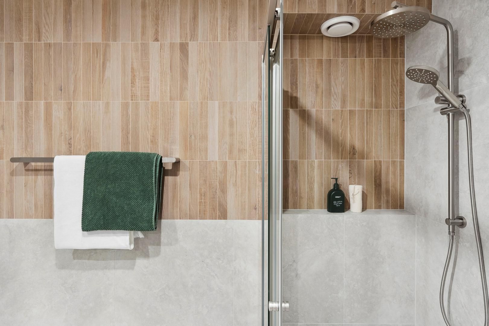 A bathroom with a shower , towel rack , and soap dispenser.