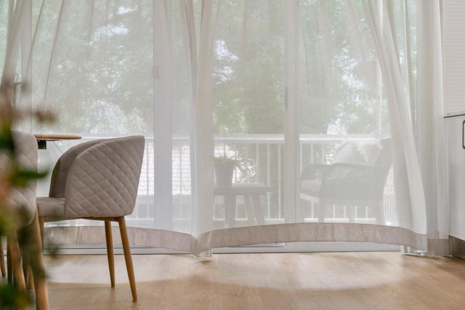 A living room with a table and chairs and a sliding glass door with white curtains.