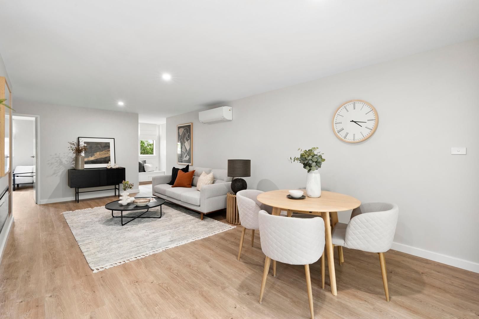 A living room with a couch , table and chairs and a clock on the wall.
