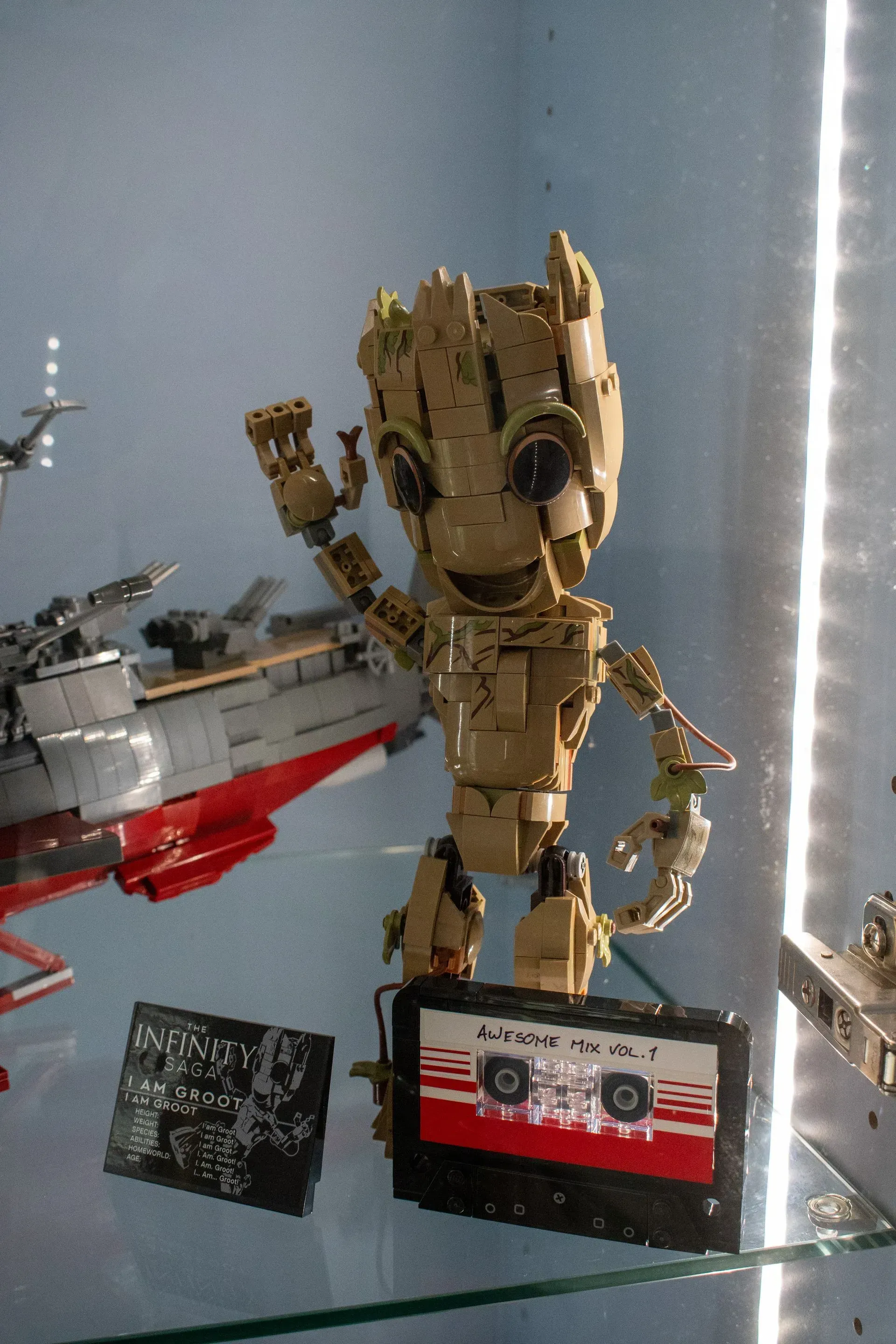 A toy groot is sitting on a glass shelf next to a cassette tape.