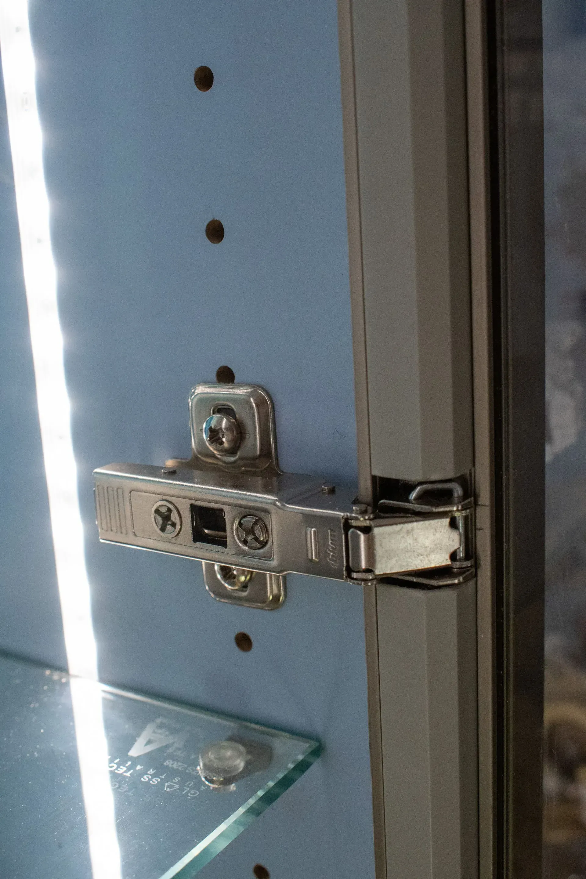 A close up of a door hinge on a cabinet with a glass shelf.