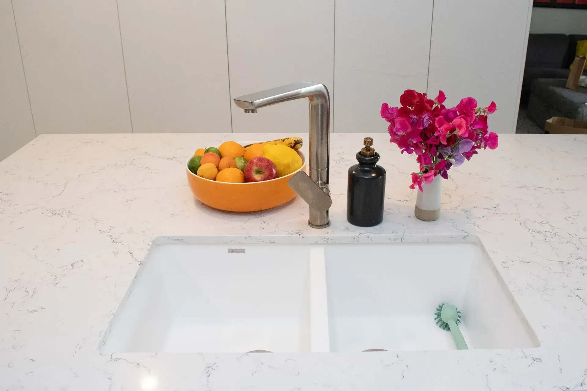 A kitchen sink with a bowl of fruit on top of it