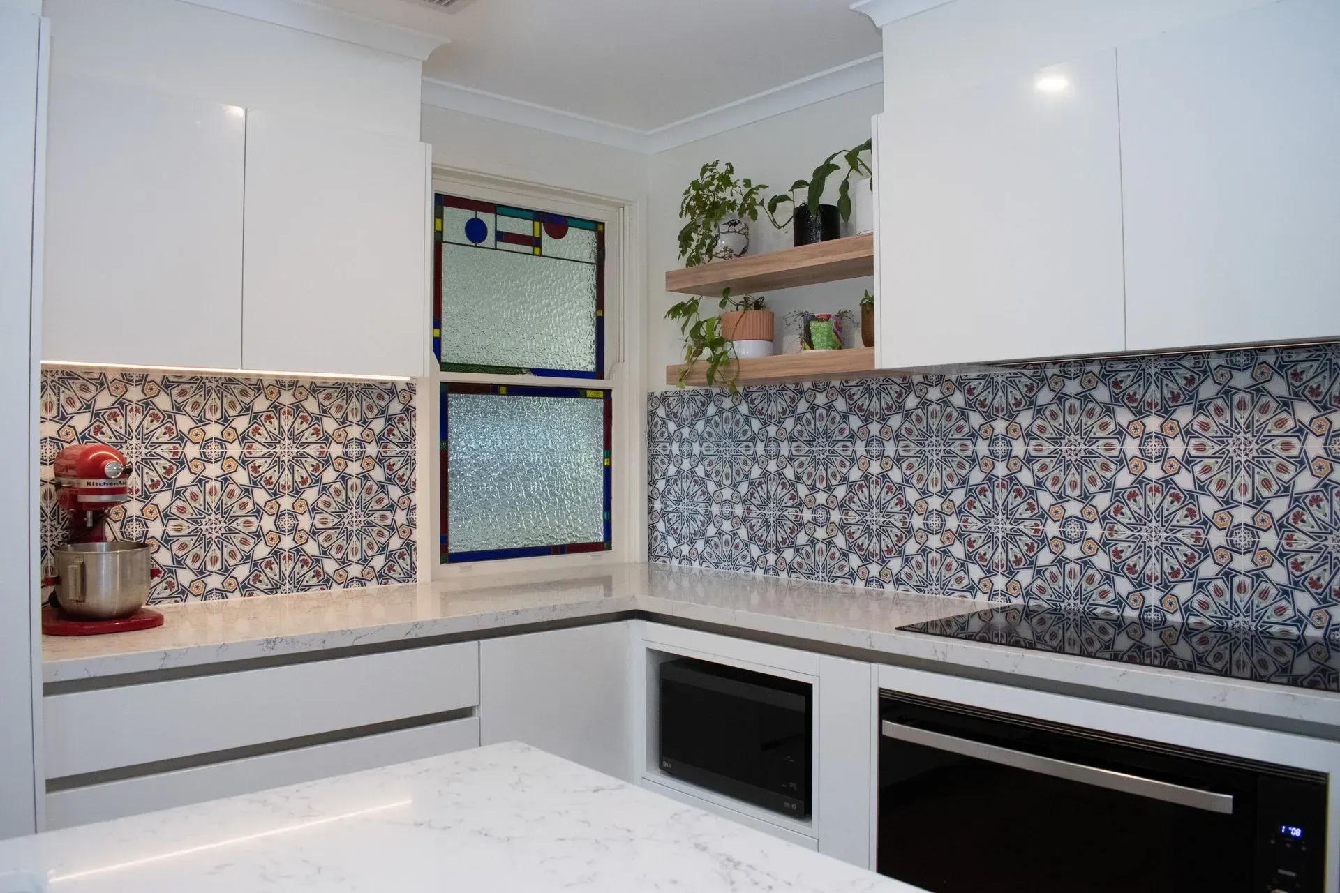 A kitchen with white cabinets , black appliances , a mixer , and a window.