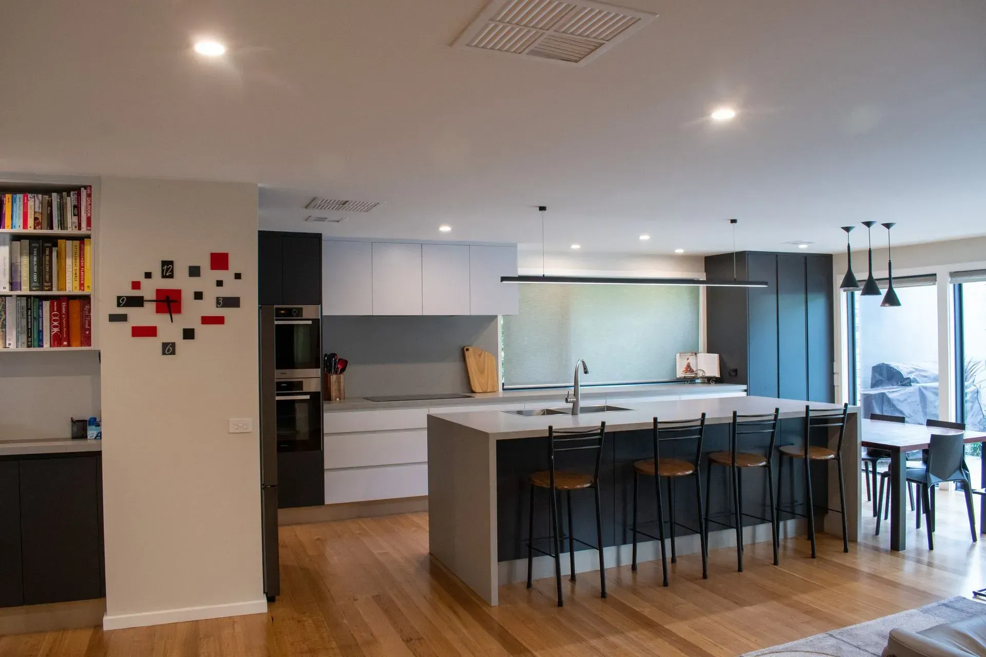 A kitchen with a large island and stools and a clock on the wall.