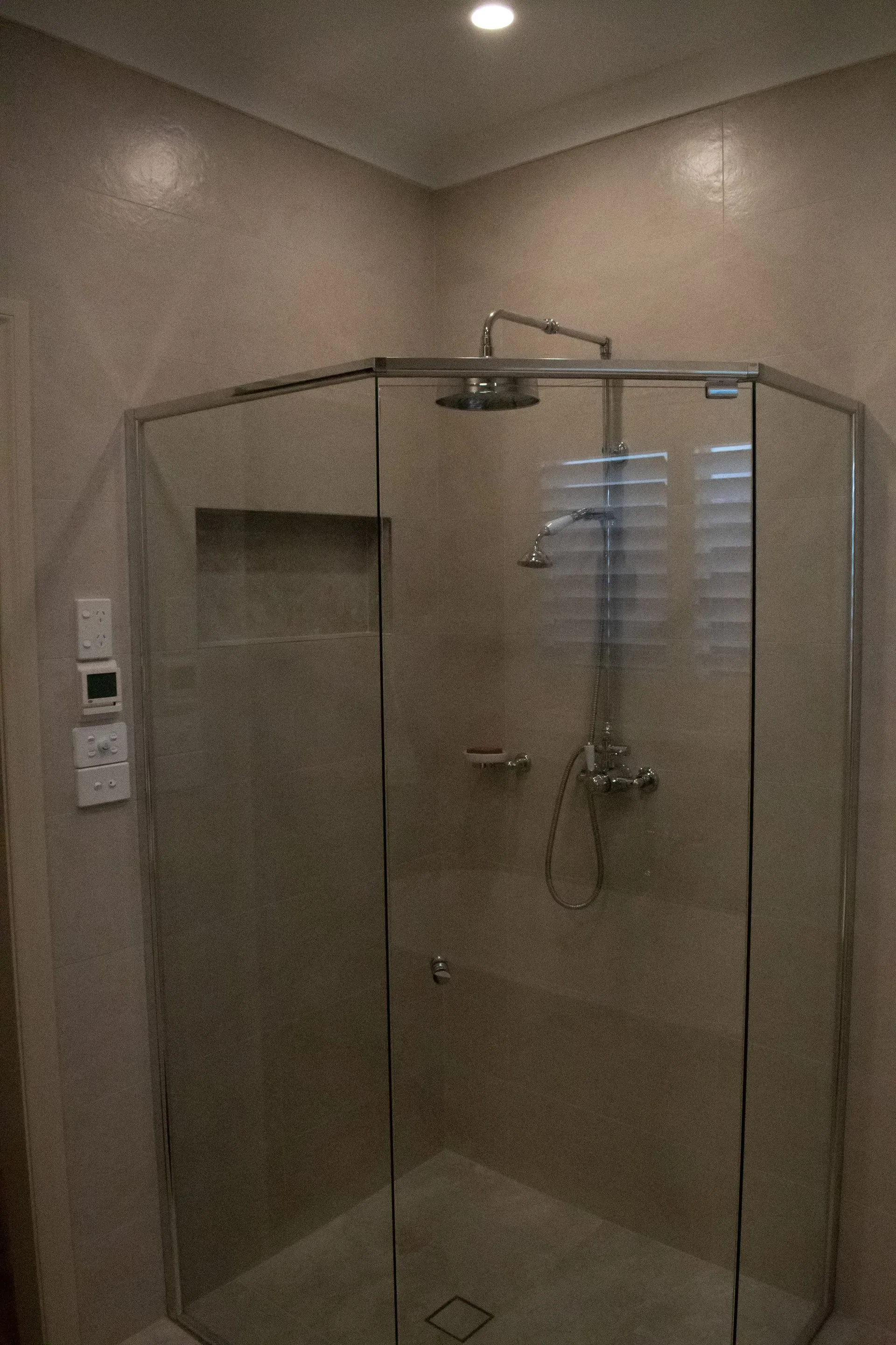 A tiled, walk-in shower stall with a niche and corner seat under construction in an unfinished room with drywall.