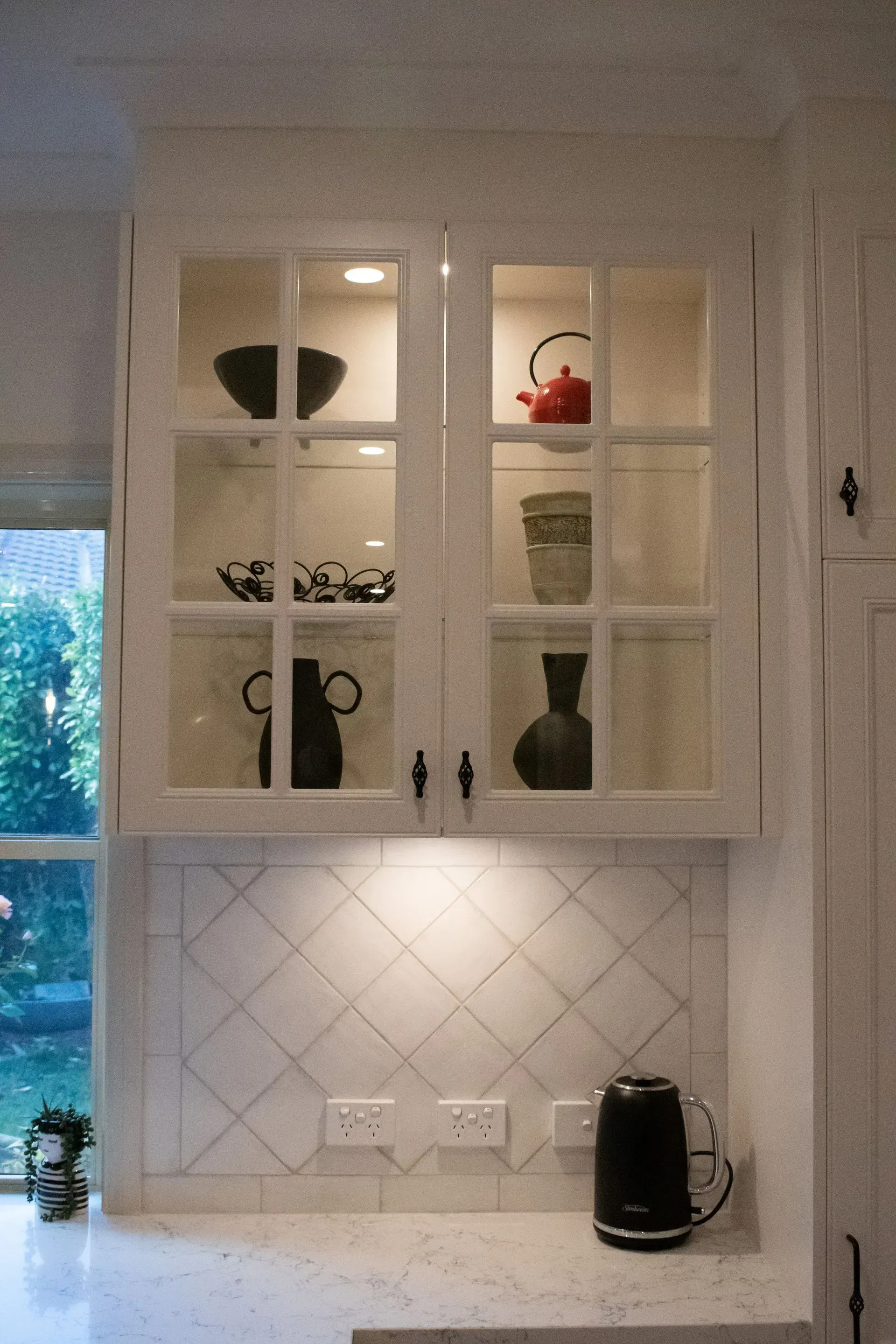 A kitchen with white cabinets and a black kettle