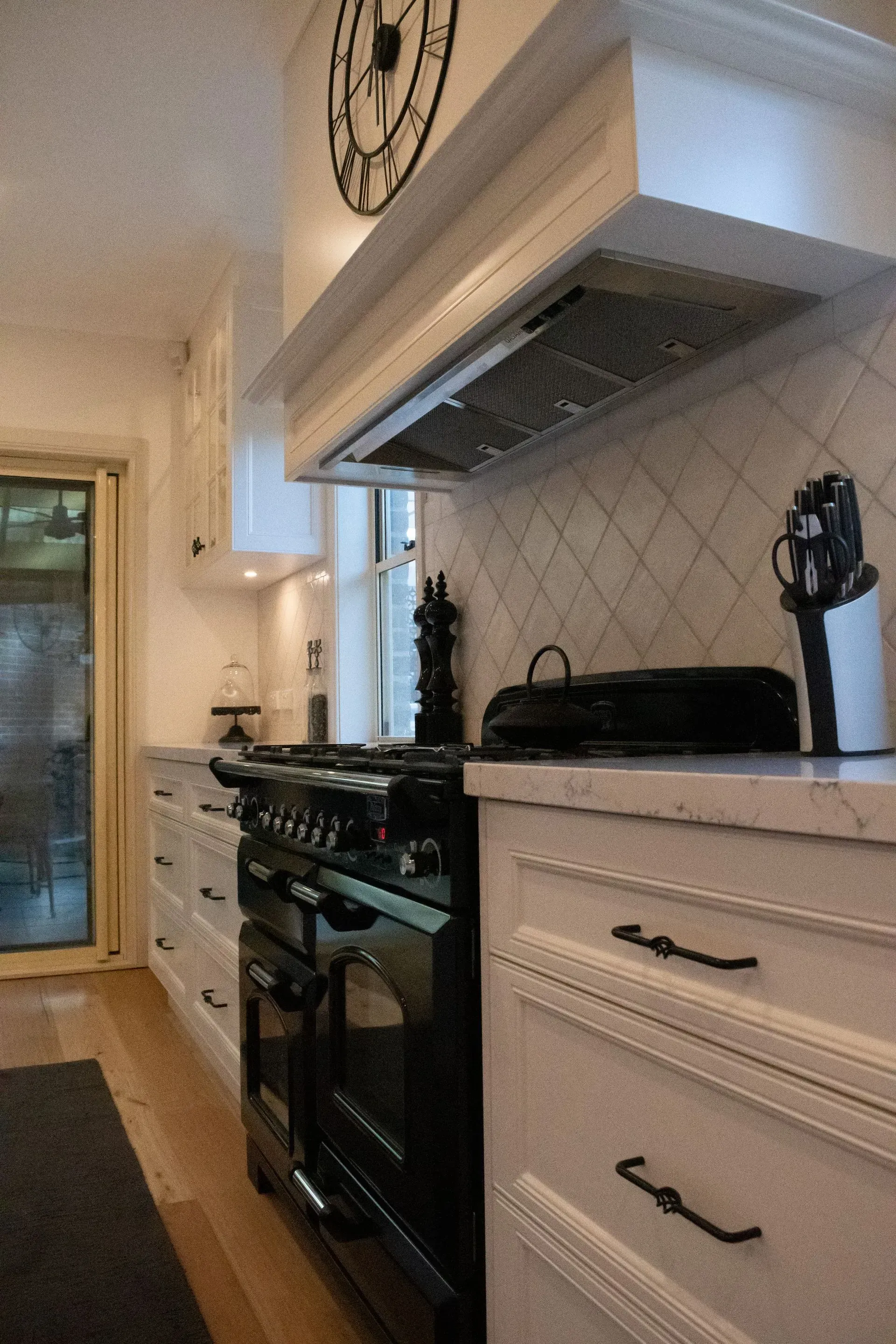 A kitchen with a black stove and white cabinets and a clock on the wall above the stove.