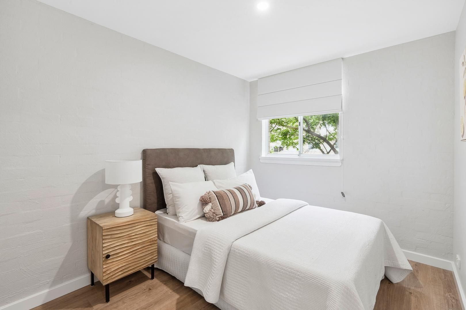 A bedroom with a bed , nightstand , lamp and window.