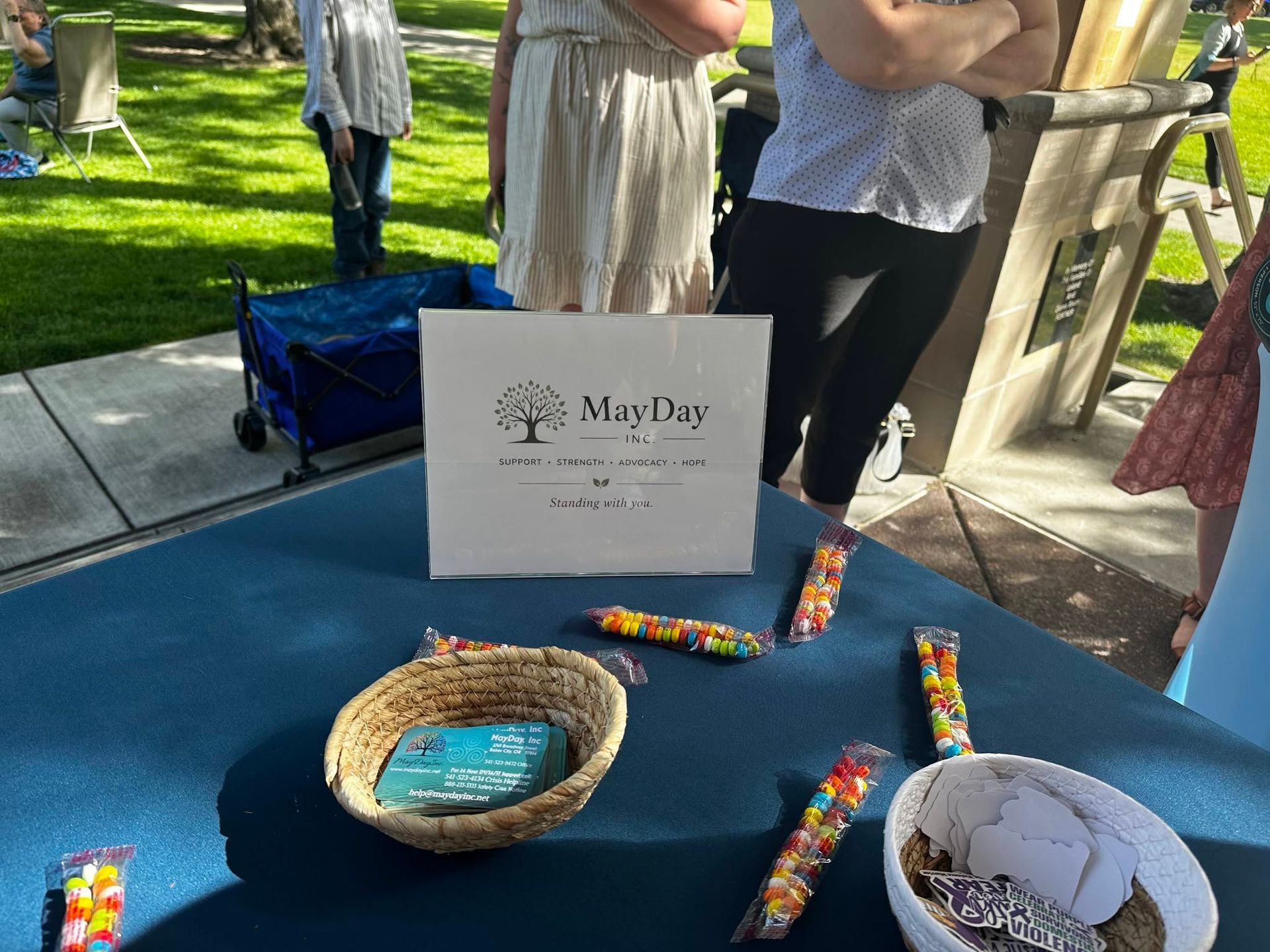 May Day display with colorful candy on a blue tablecloth, basket, and sign in a sunny outdoor setting