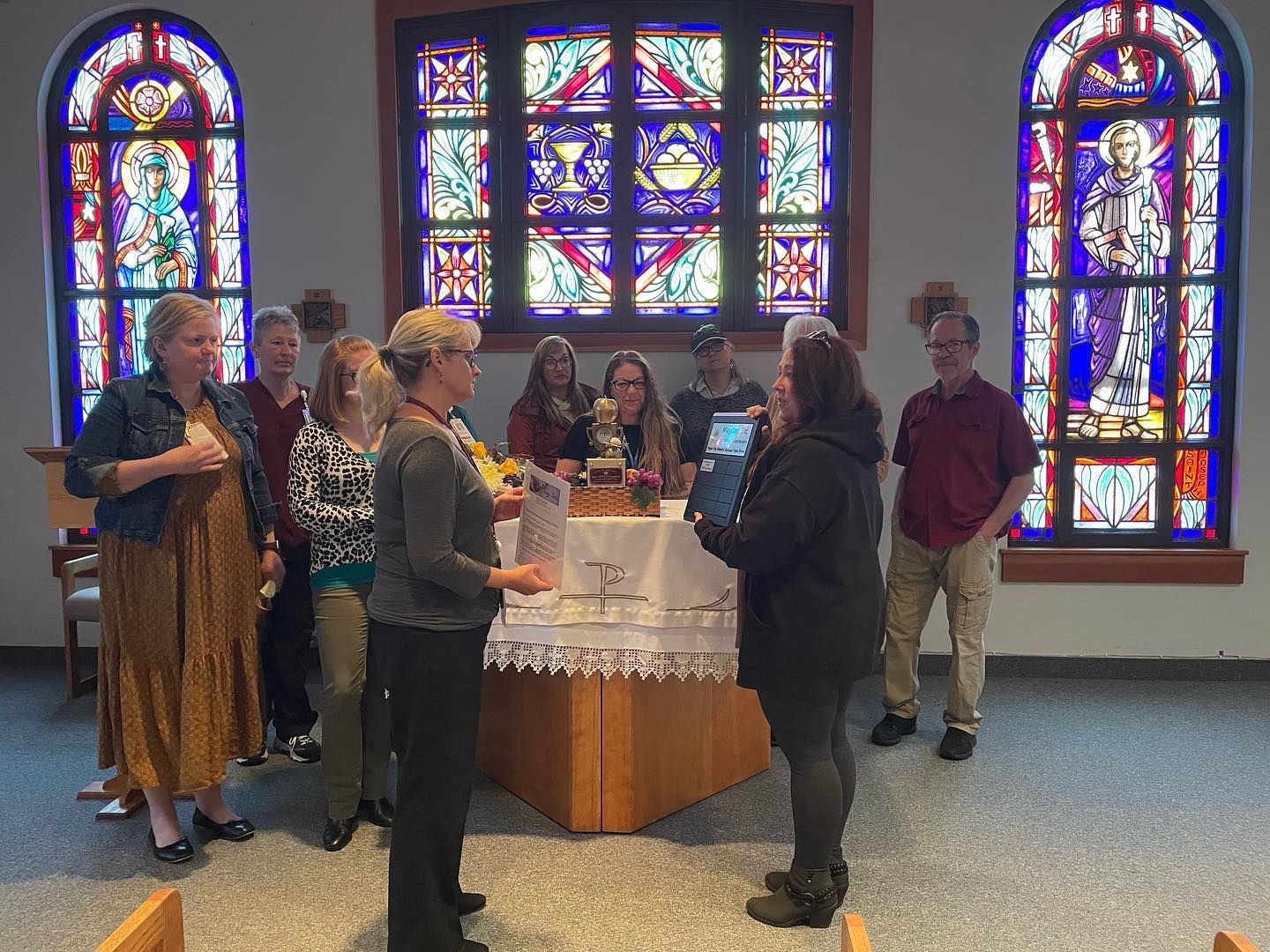People gathered around a table in a church with colorful stained-glass windows.