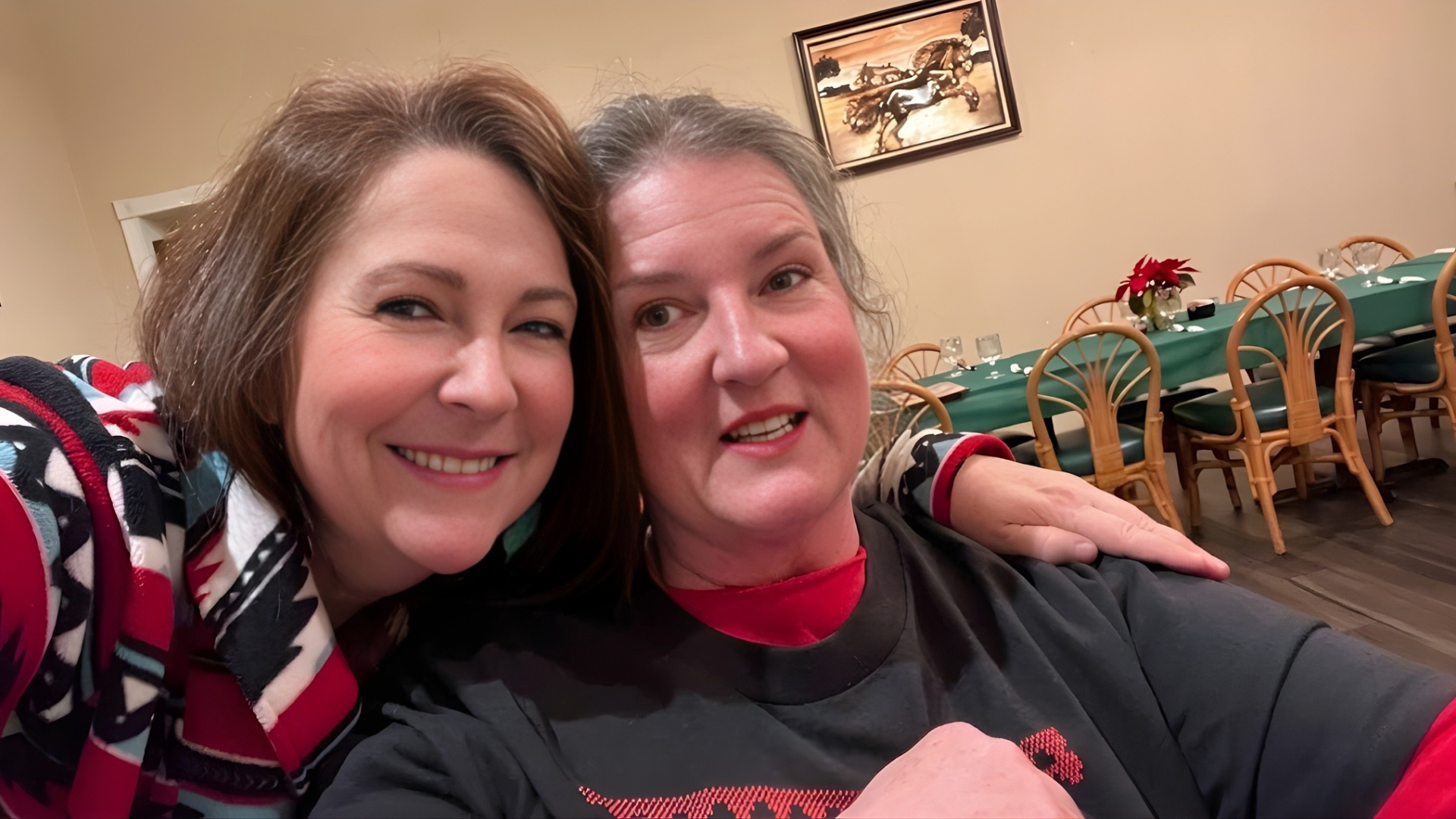 Two smiling people sitting close together in a restaurant, with tables and chairs in the background.