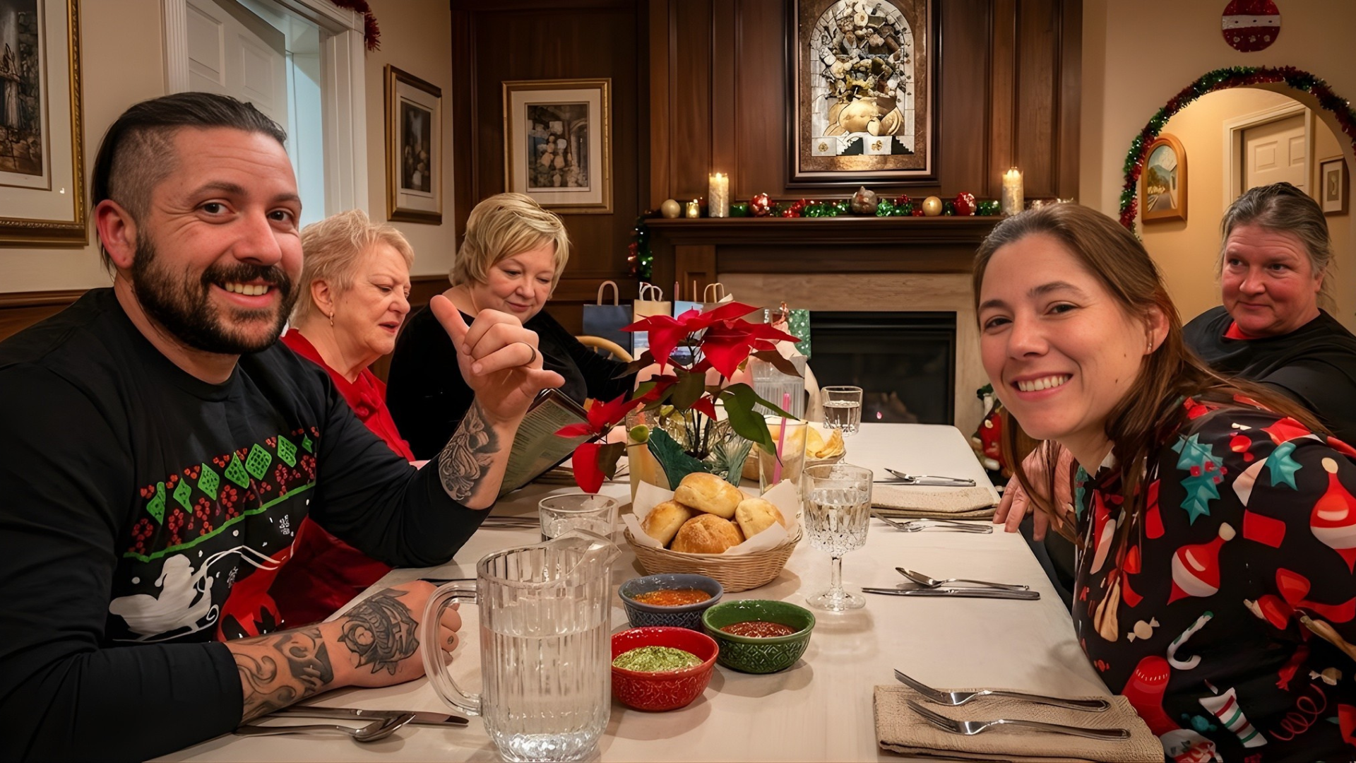 Friends smiling around a festive dining table with flowers, snacks, and holiday decor in a warmly lit restaurant