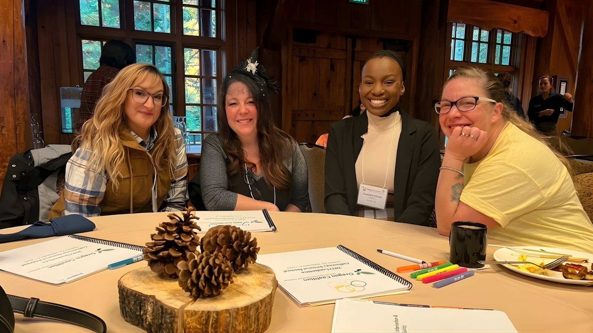 Four people smiling at a table with pinecones, papers, and markers in a cozy wood-paneled room