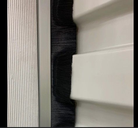 Black brush seal between a white door and silver siding panel
