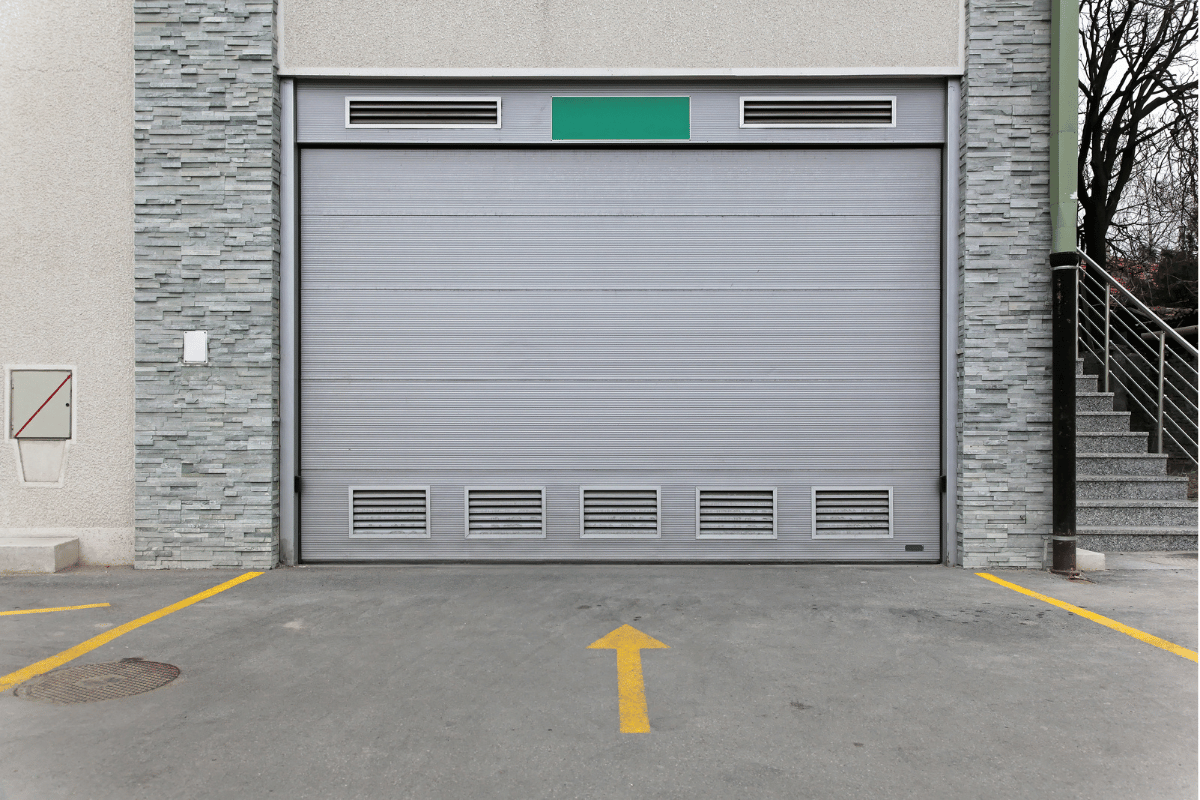 Closed gray industrial garage door with yellow arrow on concrete driveway