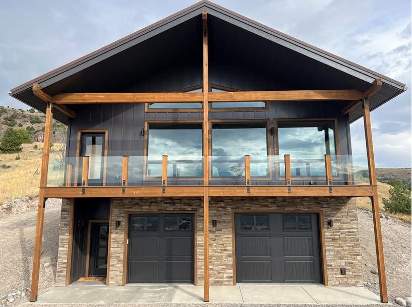 Modern two-story mountain cabin with wood balcony, glass front, and two garage doors