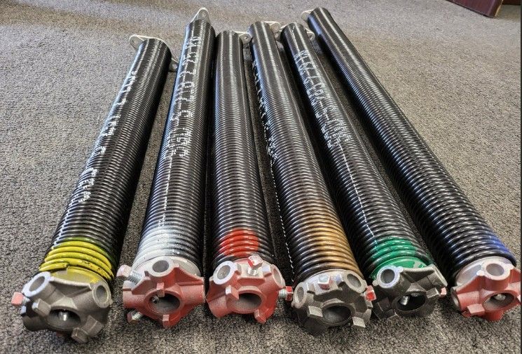 Six coiled metal springs with colored bands and fittings, lined up on a carpeted floor.