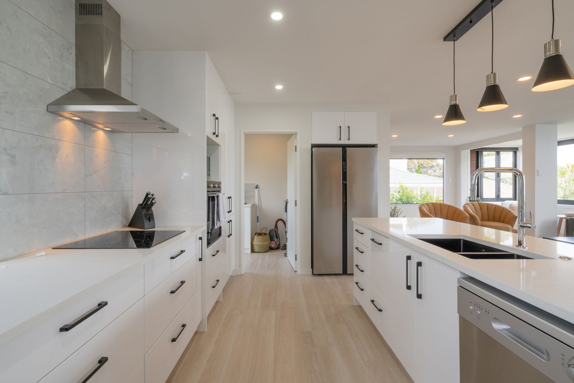 Modern white kitchen with island, stainless appliances, wood floors, and pendant lights.