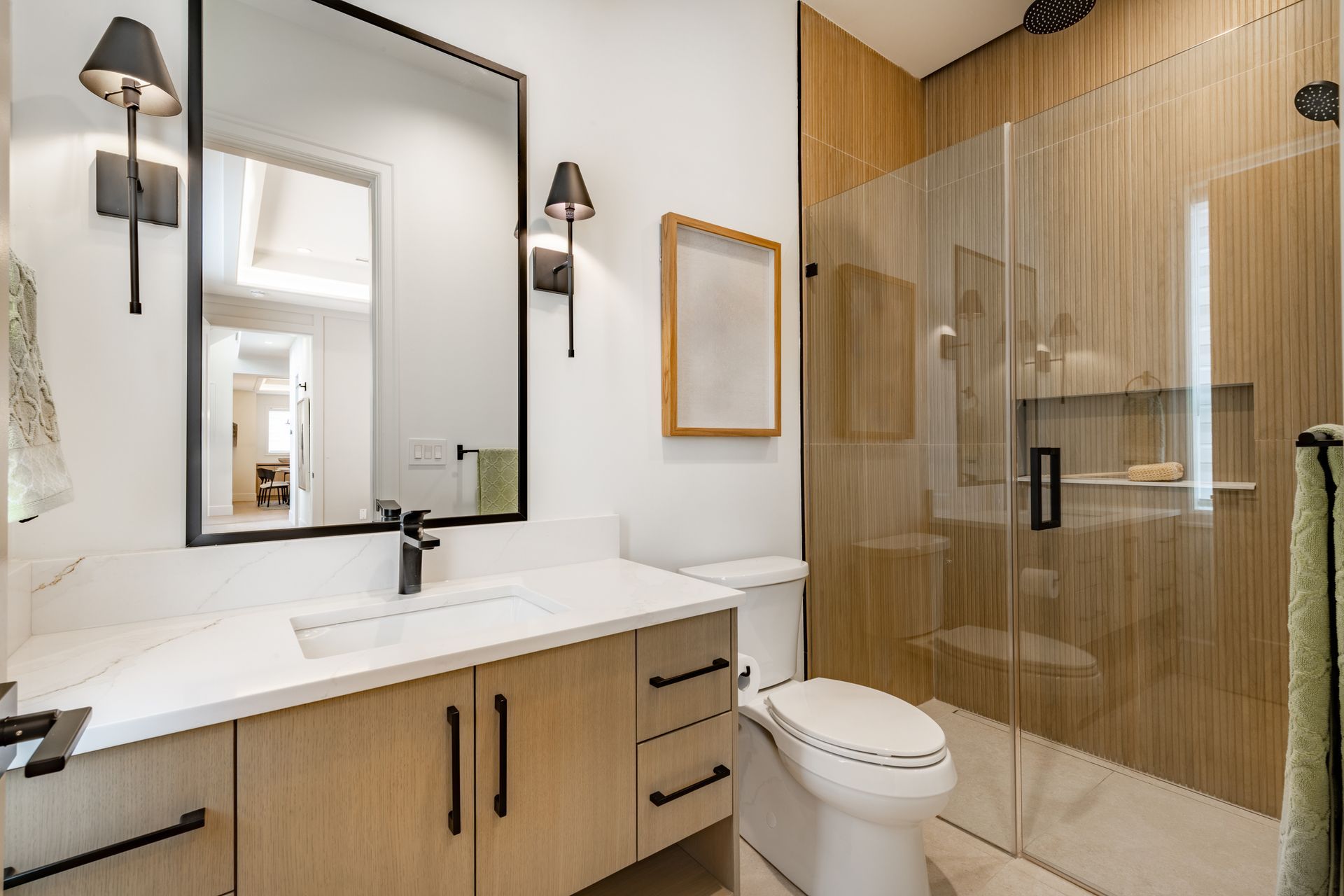 Modern bathroom with a vanity, toilet, and glass shower. Light wood and neutral tones.