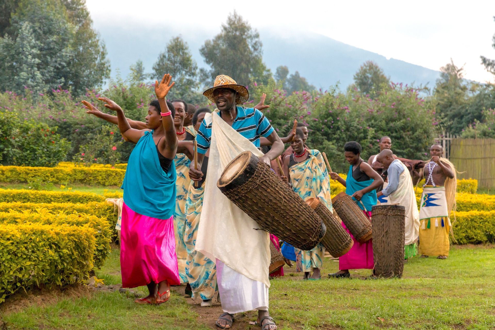 A person in a tan jacket shakes hands with a local resident wearing traditional patterned clothing in a rural setting.