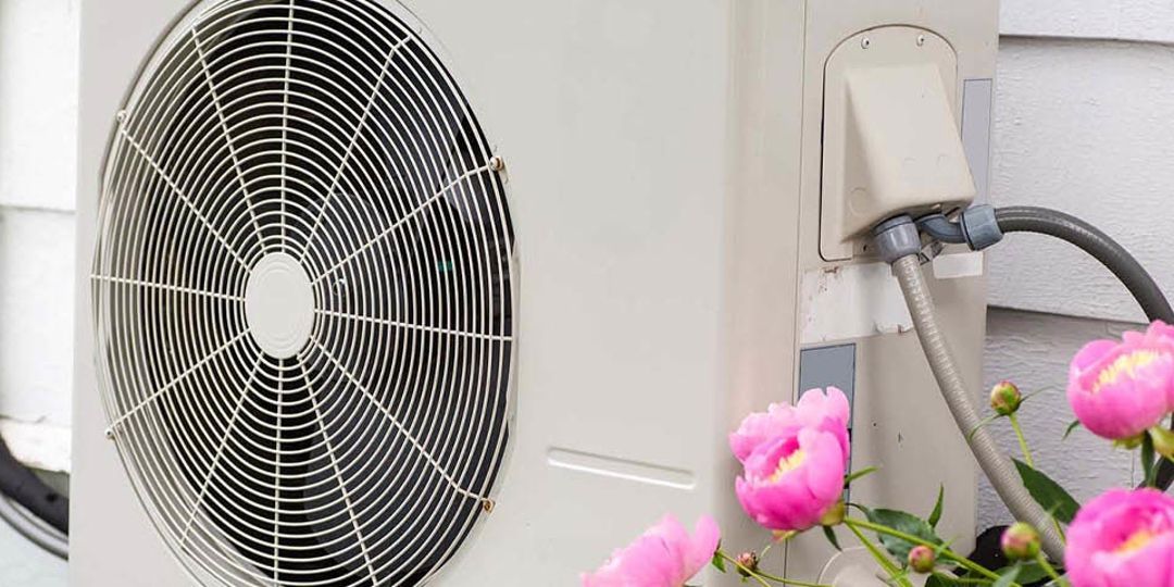 A fan is attached to the side of a building next to pink flowers.