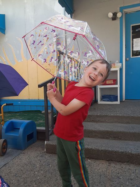 Child smiling, holding a unicorn-themed umbrella outside a blue building.
