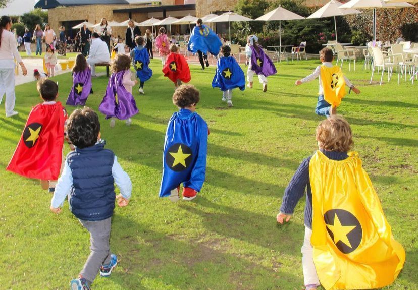 Un grupo de niños con capas de superhéroe corren por el césped.