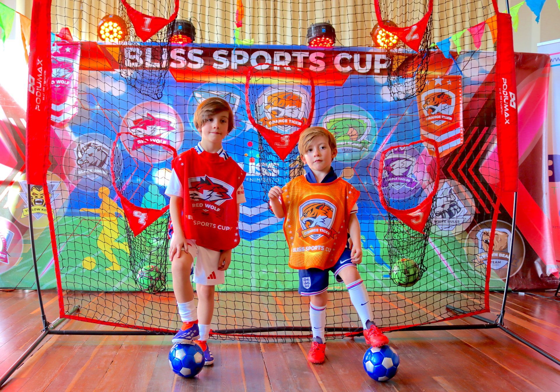 Dos niños pequeños están parados uno al lado del otro con balones de fútbol frente a una pared.