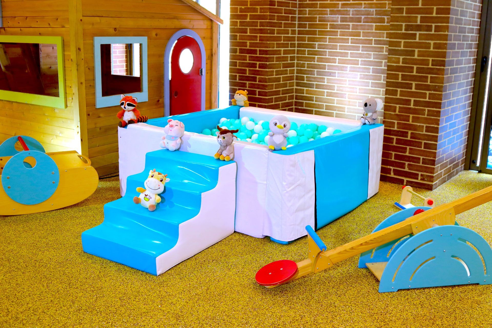 Sala de juegos con piscina de pelotas, juguetes y casita de madera.