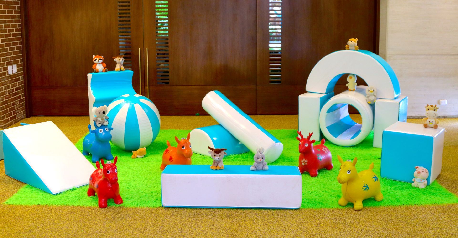 Juguetes para perros en un área de juegos, con bloques de espuma, un arco y juguetes de caballos saltarines.