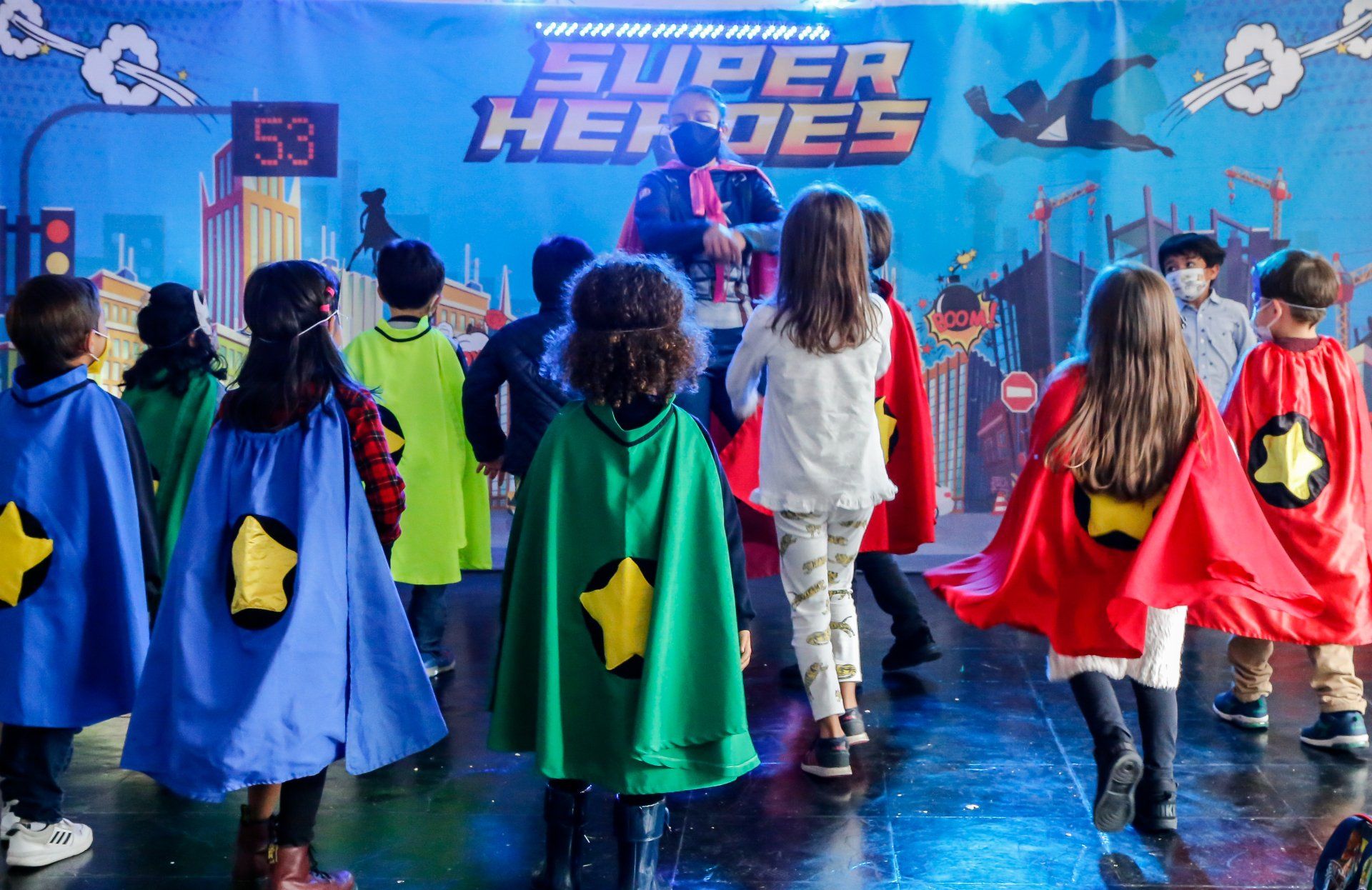 Un grupo de niños vestidos como superhéroes están bailando en un escenario.