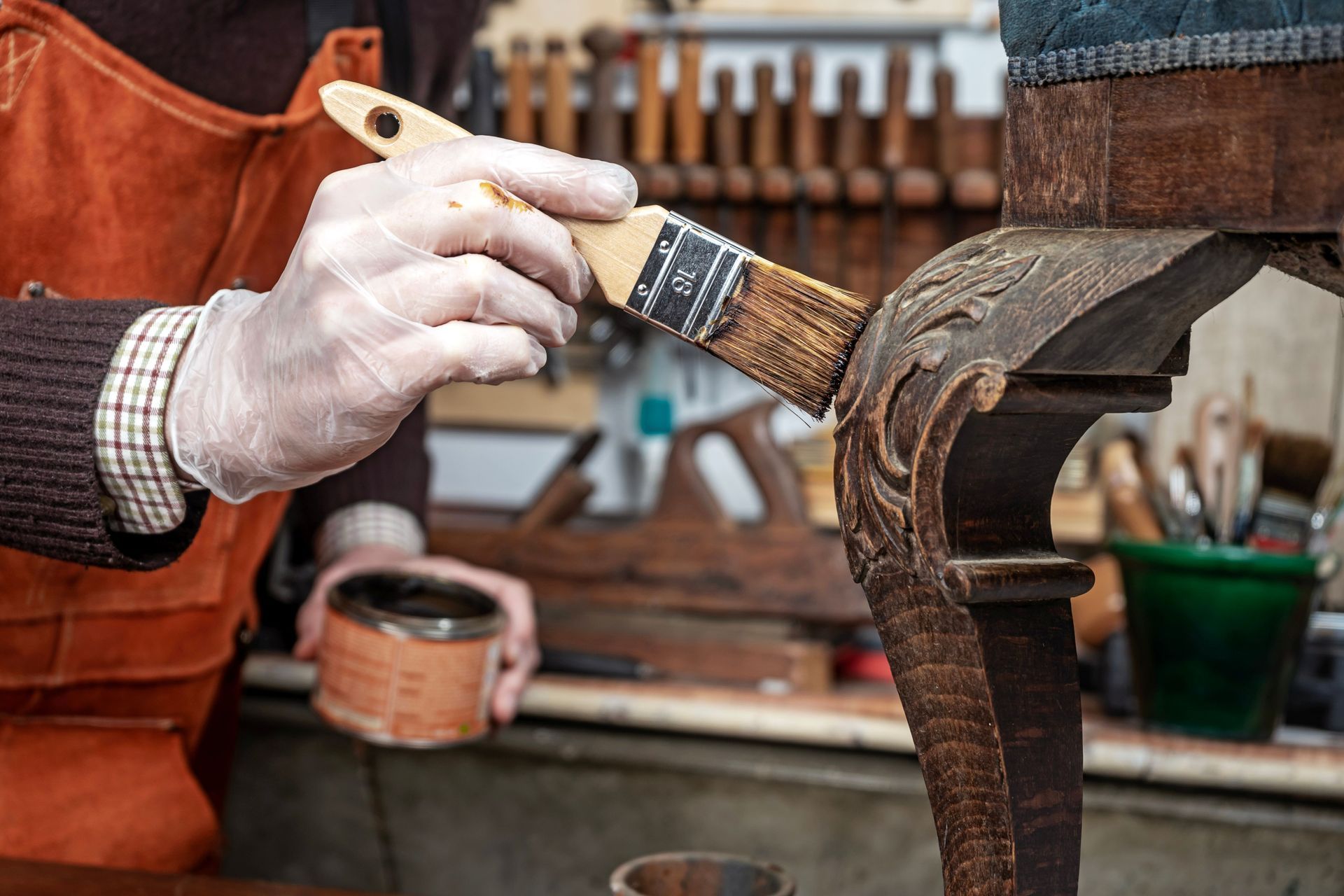 A partial view of a carpenter restoring an antique chair with wood wax and a brush. A partial view of a carpenter restoring an antique chair with wood wax and a brush.