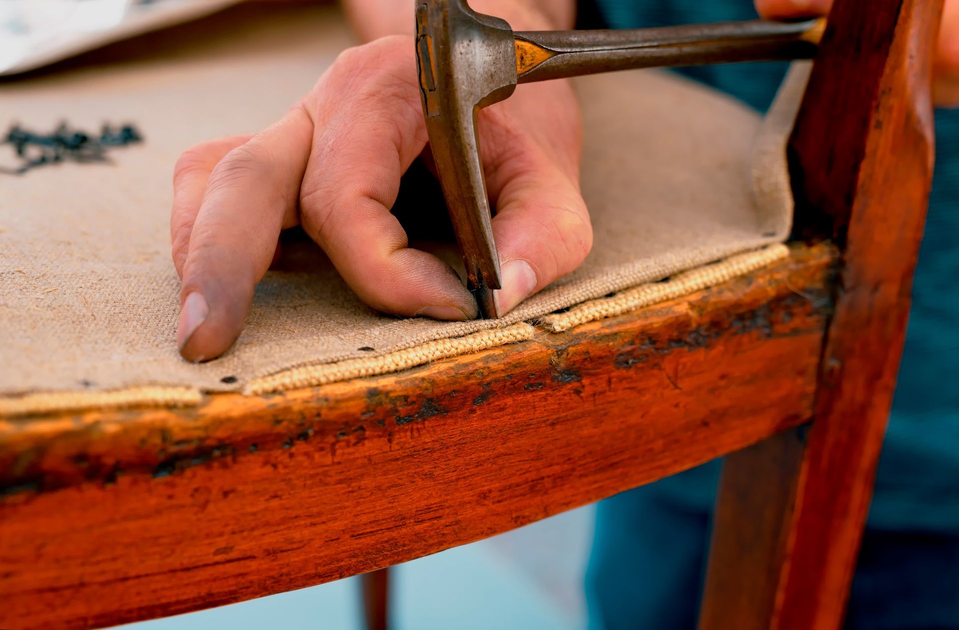 Close view of the hand of a worker with a special hammer repairing upholster of an antique chair.