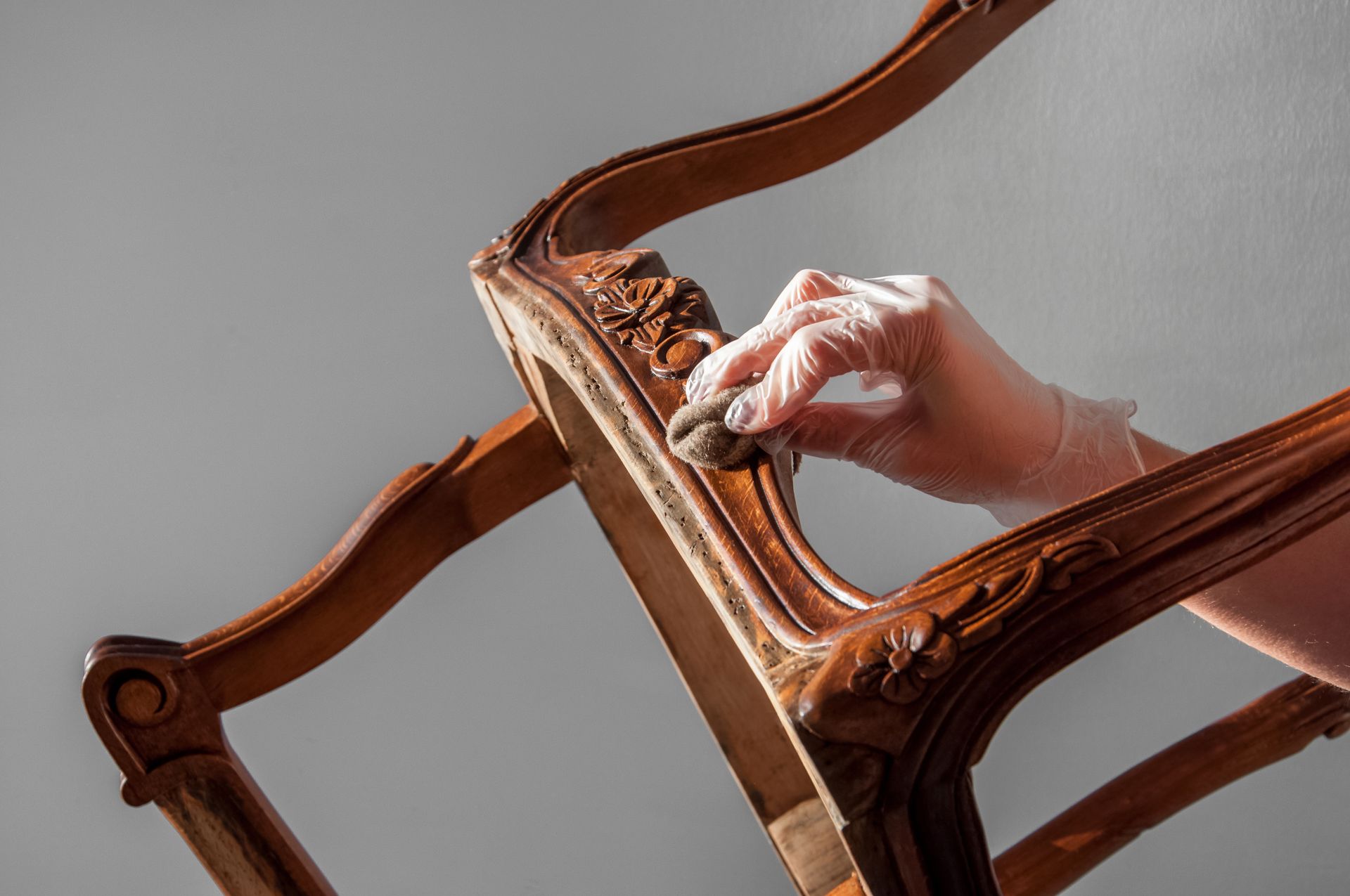 Hand wearing a glove sanding an ornate wooden chair frame Hand wearing a glove sanding an ornate wooden chair frame